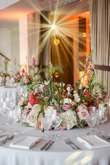 Elegant wedding table setup with soft pink floral centerpiece, crystal glassware, and glowing ambient light creating a romantic, luxurious atmosphere for a fine dining celebration.