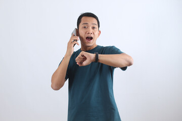 Shocked Asian man checks watch while on phone call, running late