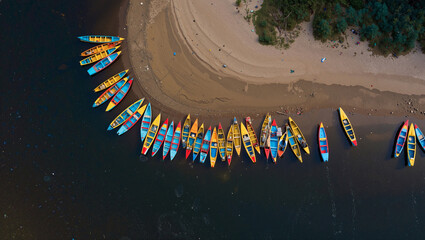 Brightly colored boats lined along a sandy riverbank create vibrant contrast with dark water on a sunny day. Generative AI.