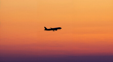 Obraz premium Single airplane silhouette flying high across a vibrant gradient sky during a dramatic orange sunset