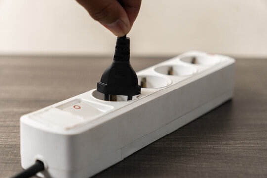 White Power Strip with Black Plug Being Unplugged by a Hand