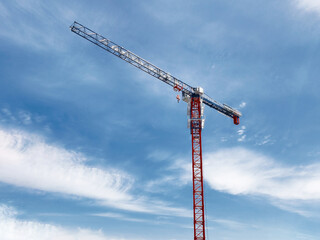 Construction crane rises high against the blue sky at a building site in mid-afternoon under fluffy white clouds