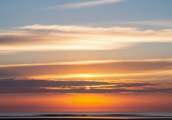 Obraz premium A stunning high-resolution photograph of a partly cloudy sky at sunrise. The horizon glows with soft pink, peach, and golden tones blending into a light blue upper sky. Fluffy, diffused clouds catch t