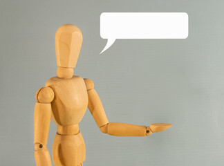Wooden mannequin gesturing with hand extended and speech bubble on gray background