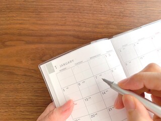 A woman's hands filling out a January schedule book on a wooden table