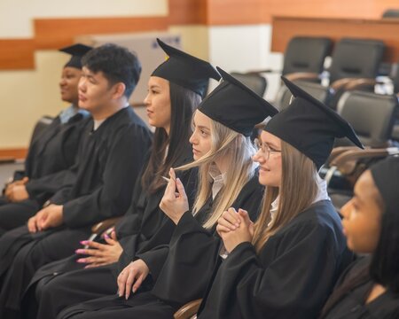 Graduates sit on a bench, listen to the speech and applaud. 
