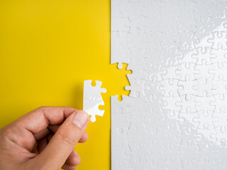 Concept of solving and completing a mission with hand placing the last puzzle piece on yellow...