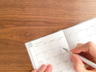 Woman's hand filling out a January schedule book on a wooden table