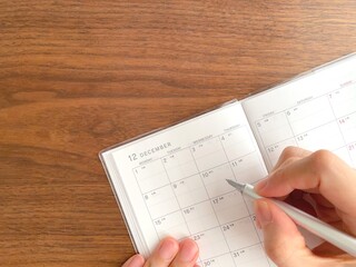 Woman's hand filling out a December schedule book on a wooden table