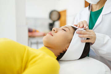 Fototapeta premium A woman is getting her face massaged by a man in a white lab coat. The woman is wearing a yellow sweater and the man is wearing gloves. The scene is set in a medical setting 