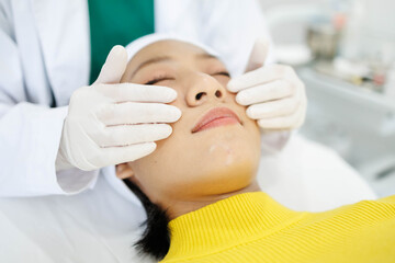 Obraz premium A woman is getting her face massaged by a man in a white lab coat. The woman is wearing a yellow sweater and the man is wearing gloves. The scene is set in a medical setting 