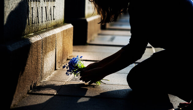 A solitary figure honors a memory, placing a blue bouquet on a sunlit gravestone