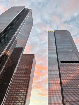 LOS ANGELES, CA, SEP 21, 2025: three skyscrapers reach upward against pastel sunset clouds. Rear left tower shows dark glass while front buildings have lighter, blue-ish glass windows