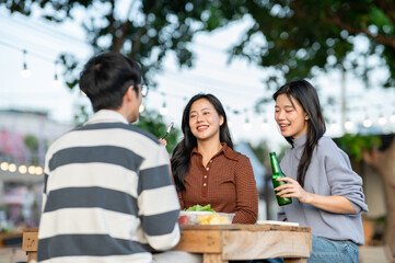 Asian woman holding bottle and friends eating fruit while sitting at table in campground restaurant.
