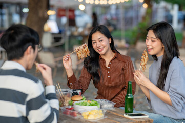 Asian woman holding eating meat skewer with friend while sitting at table in a campground restaurant