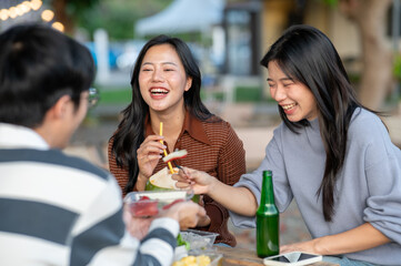 Asian woman drinking fresh coconut water with friends eating foods at table in campground restaurant