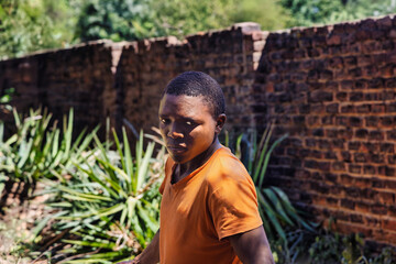 single young african man with a tough look walking in the yard, wearing an orange t-shirt