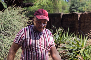 single young overweight african man laborer walking in the yard, wearing an striped t-shirt and a cap