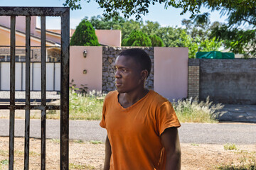 african man standing in front of gate with metal bars, he got a manly rough face
