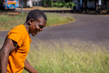 single happy young african man walking on the street at a curve, waring a orange t-shirt