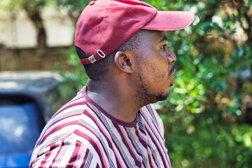 single young overweight african man walking in the yard, wearing an striped t-shirt and a cap