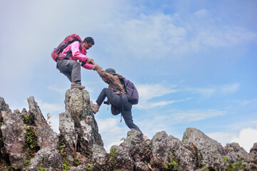 Two hikers on rocky mountain peak helping each other climb, symbol of teamwork, leadership, support, adventure, success, trust, exploration and outdoor lifestyle motivation in nature.