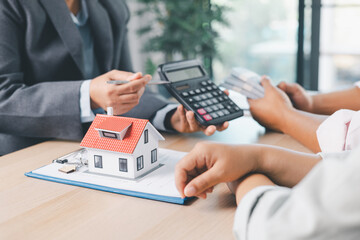 Close up of real estate agent handing house model to client with calculator and contract paperwork on desk, concept of mortgage loan, home ownership, property investment and housing agreement.