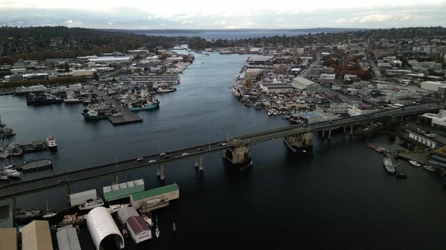 Aerial drone view of Ballard Bridge and Fishermen&rsquo;s Terminal in Seattle showing fishing boats, docks, and shipyards along the Ship Canal leading toward Puget Sound.