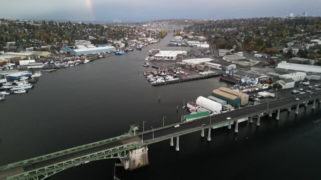 Aerial drone view of Ballard Bridge and Fishermen&rsquo;s Terminal in Seattle showing fishing vessels, docks, and the Ship Canal leading toward Lake Union under overcast light.