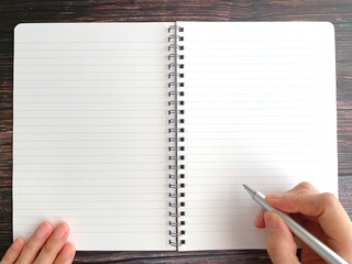 Woman's hand holding an open notebook and a ballpoint pen at a desk