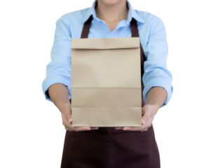 A person in an apron holds out a brown paper bag, ready for delivery or takeout.