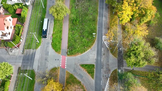 Top-down drone shot of a modern tram or bus crossing tram tracks at an intersection. A cyclist stops on a red bike path. Urban transport in autumn.