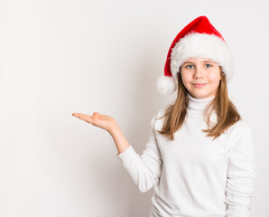 Smiling preteen girl in Santa hat and white sweater holding open palm, isolated on white. Perfect for Christmas advertising, holiday greeting, or festive copy space concepts.