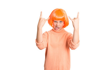 Playful preteen girl in bright orange wig and sweater showing rock hand signs and sticking out tongue, isolated on white. Perfect for fun, energy, attitude, or youth expression concepts.