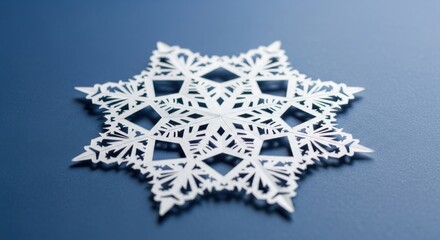 Intricate white paper snowflake cutout resting on a smooth blue surface, showcasing delicate patterns and craftsmanship, perfect for winter-themed designs and decorations