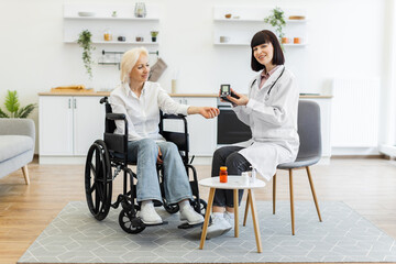 A doctor is checking the blood glucose level of a senior woman in a wheelchair at home. The doctor is holding a blood glucose meter.