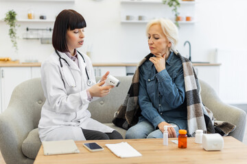 A female doctor is checking an elderly patient's temperature using a digital thermometer while the...
