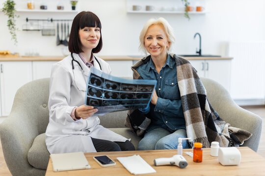 A female doctor shows an older woman her medical scan results while sitting on a sofa. They both smile, indicating a positive interaction. - Powered by Adobe