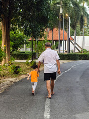 Back view of elderly father and little son or grandfather and grandson walking together at garden. Middle age father with son or senior grandfather with grandchild spending time together in park.