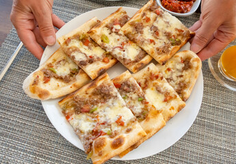 Delicious Turkish flatbread topped with minced meat and cheese served on a plate at a cozy dining table