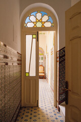 Interior of old Tangier house with tiled floor, decorated doorway, and narrow passageway reflecting Moroccan heritage.
