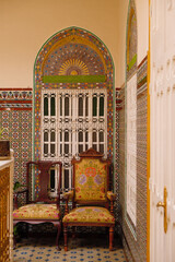 Traditional Tangier house interior with patterned tiles, ornate window, wooden chairs and historic Moroccan design elements.