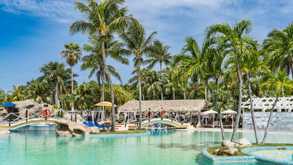 Swimming pool, tropical resort. Pedestrian arch bridges with rope railings and lifebuoys over turquoise water. Deck chairs, sun umbrellas. Palm trees against the blue sky, clouds.Cuba. Varadero. Hotel
