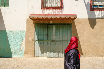 Traditional doorway with canopy against green and white-orange wall in Tangier, with a local woman walking past.