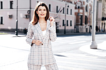 Fototapeta premium Portrait of young beautiful brunette woman wearing nice trendy plaid suit jacket. Sexy smiling model posing in the street at sunny day. Fashionable female outdoors. Cheerful and happy.