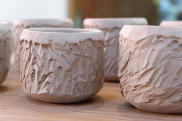 A collection of freshly shaped clay pots with textured surfaces arranged on a wooden table. The pottery is still in its raw state, displaying detailed patterns and craftsmanship. 