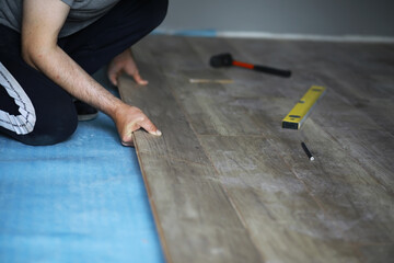 Installing laminated floor, detail on man hands blue wooden tile, over white foam base layer, small pile with more tiles background