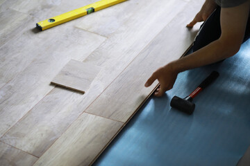 Installing laminated floor, detail on man hands blue wooden tile, over white foam base layer, small...
