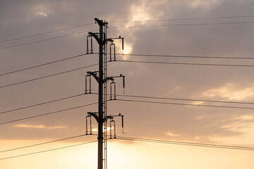 power transmission tower with multiple lines stands against a sunset sky with scattered clouds