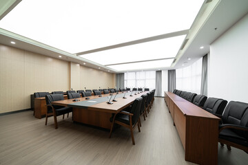  large conference room with a long wooden table, black chairs, microphones, and a bright ceiling...